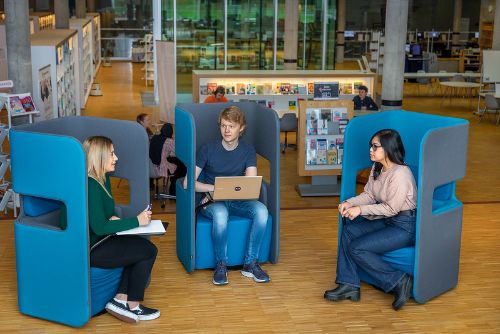 Tre studenter sitter i biblioteket og prater sammen