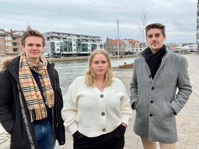 De tre prosjektdeltakerne står ved vannkanten med Fredrikstad sentrum i bakgrunnen. 