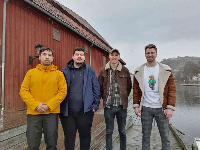 The four project members Isak Bamiani, Khayam Nami, Kjell Randby Kristensen and Ole Kristian Eriksen Nysted standing on a pier. 