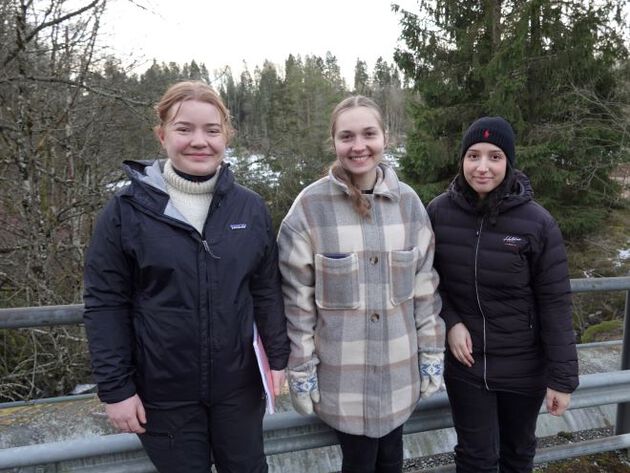 De tre prosjektdeltakerne Anna Emilie Løe, Ronja R. Eivarr og Nora Hamzaoui står ved siden av hverandre på en vei med skog i bakgrunnen.