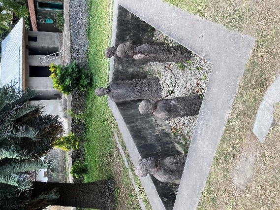 The photograph shows separate statues of four people who are standing in a sunken area surrounded by a wall, and are chained together.