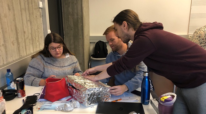 Her ser vi tre studenter (en jente og to gutter) som arbeider med sitt entreprenørskapsprosjekt. De holder på å kle en eske med aluminiumsfolie.
