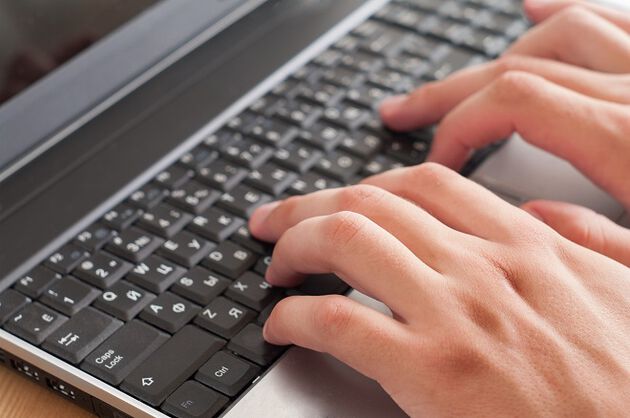 Bildet viser et nærbilde av et tastatur på en laptop, med to hender som skriver.