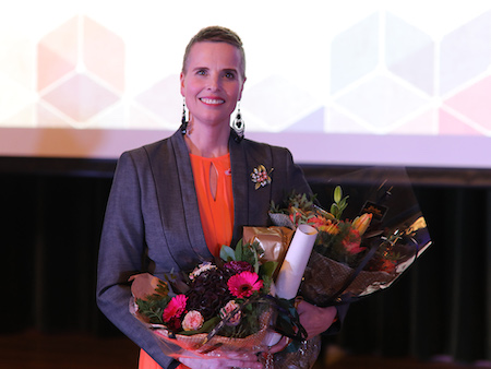 Bildet av Høeg Karlsen stående på scenen med blomster på den akademiske årsfesten. 