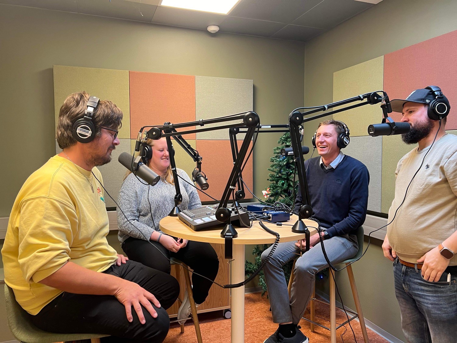 viser fire lærere som sitter rundt et bord med mikrofoner og hodeltelefoner i et podkast studio