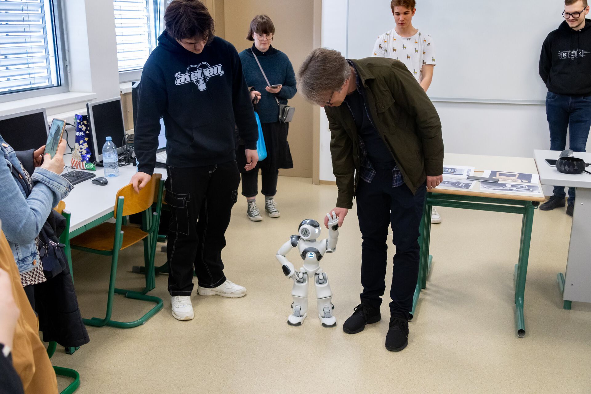 Student and teacher holding hands with a small robot in a classroom