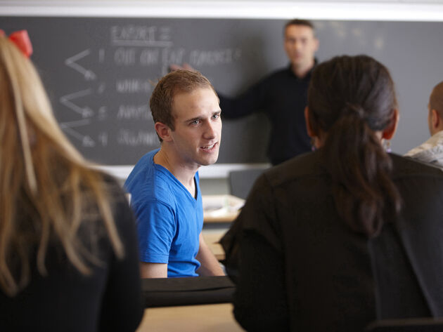 Bilde viser to personer i en dialog i et klasserom med flere mennesker