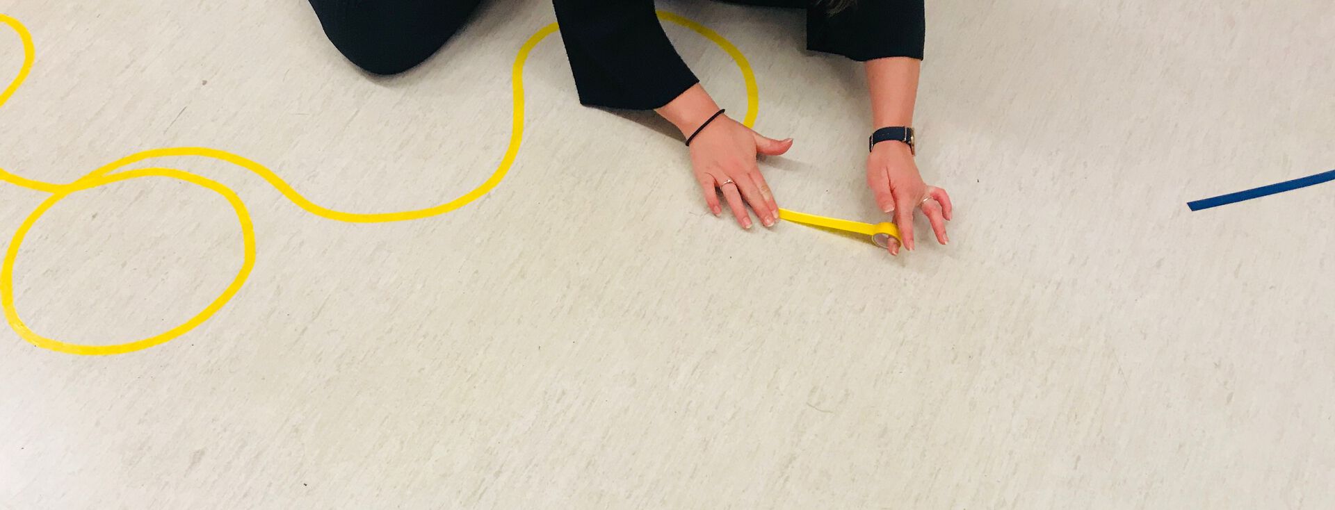En person sitter på gulvet og limer gul tape på gulvet. 