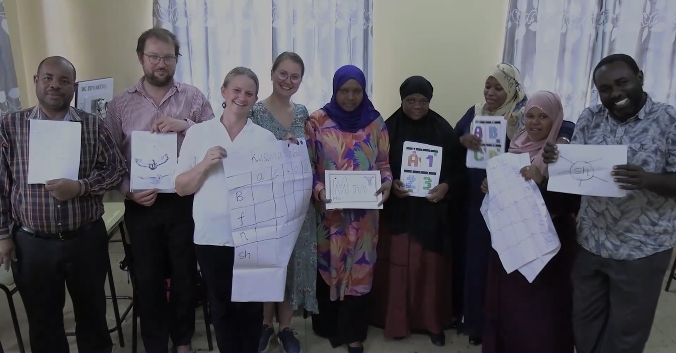 The photo shows the nine project participants in NoZa. Everybody is holding a paper in the hand.