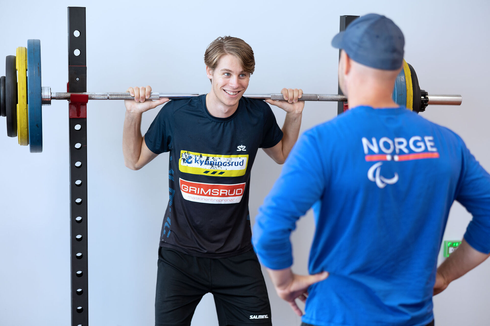 Bildet viser ung mann som løfter tunge vekter med assistent fra Olympiatoppen ved sin side